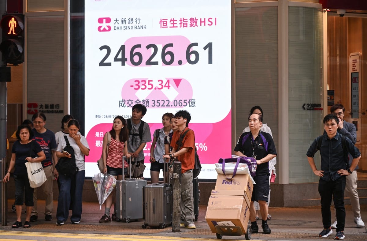 Pedestrians wait to cross a street in front of an electronic sign board showing the Hang Seng Index in Hong Kong on June 8, 2026. (Photo by Peter PARKS / AFP)