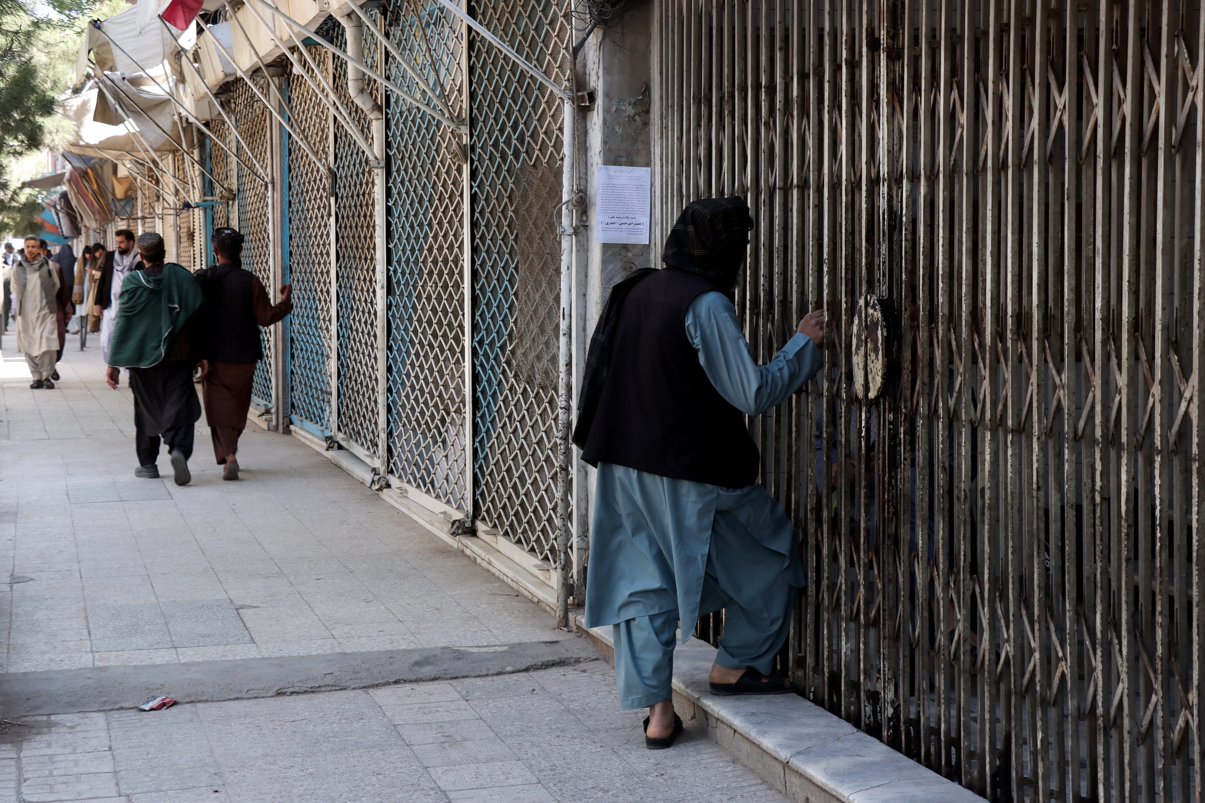 Afghan men walk past shops closed in solidarity with victims killed in an attack by unidentified armed men on the outskirts of the Sayed Mohammad Agha Shia shrine, a day after the incident in Herat on April 11, 2026.