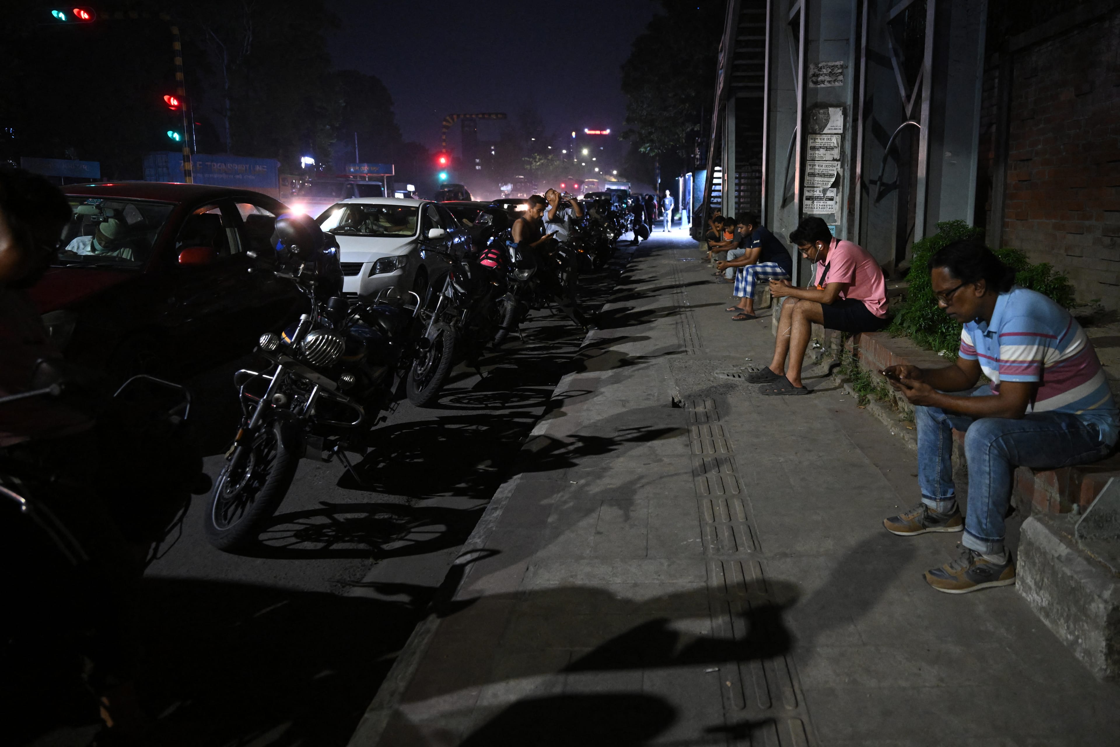 People queue up along a road, to refuel their vehicles at a filling station in Dhaka on April 21, 2026 amid Bangladesh's fuel crisis triggered by the Middle East war. (Photo by MUNIR UZ ZAMAN / AFP)