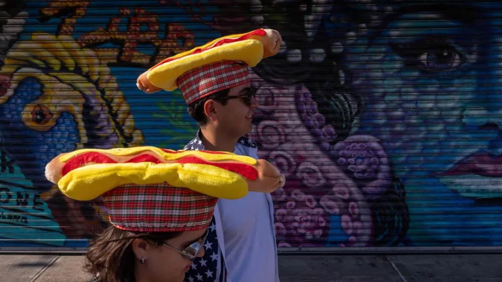 Two people wearing hotdog hats line up to watch Nathan's Annual Hot Dog Eating Contest on July 4, 2025 in the Brooklyn borough of New York City. (AFP)