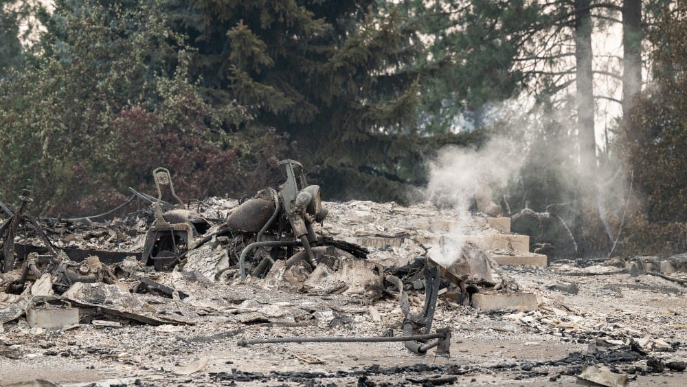 A burned motorcycle sits in the ashes of burned out residential home in the Balboa neighborhood of Spokane, Washington, on August 2, 2026. Fast-moving fires left a trail of destruction in the northwestern US city of Spokane on Sunday, with officials repor