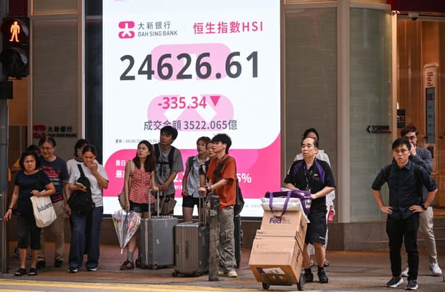 Pedestrians wait to cross a street in front of an electronic sign board showing the Hang Seng Index in Hong Kong on June 8, 2026. (Photo by Peter PARKS / AFP)