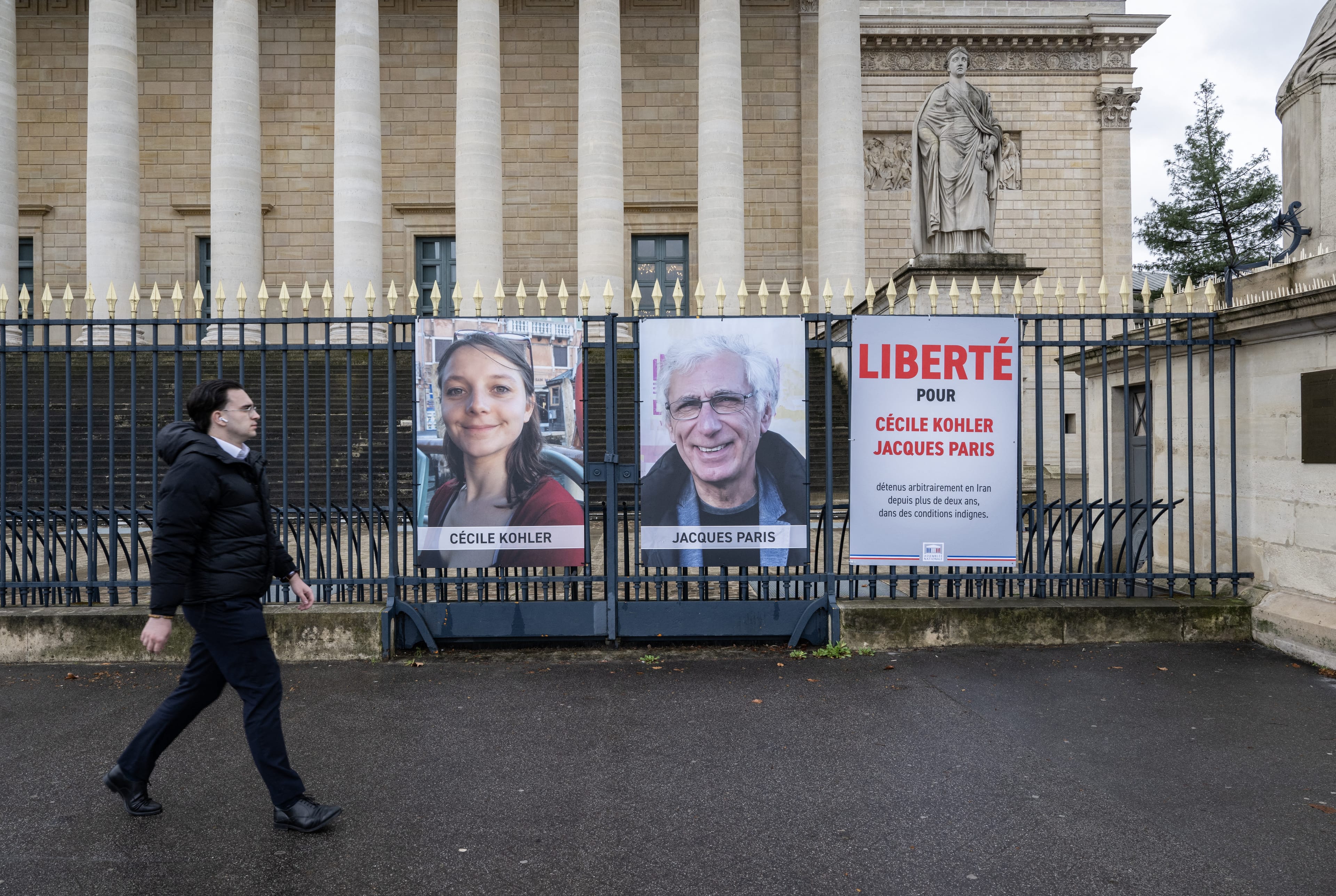 A pedestrian walks past portrait placards of Cecile Kohler and Jacques Paris, two French citizens formerly detained in Iran, set up on a fence of the French National Assembly, in Paris on March 11, 2026. (AFP)