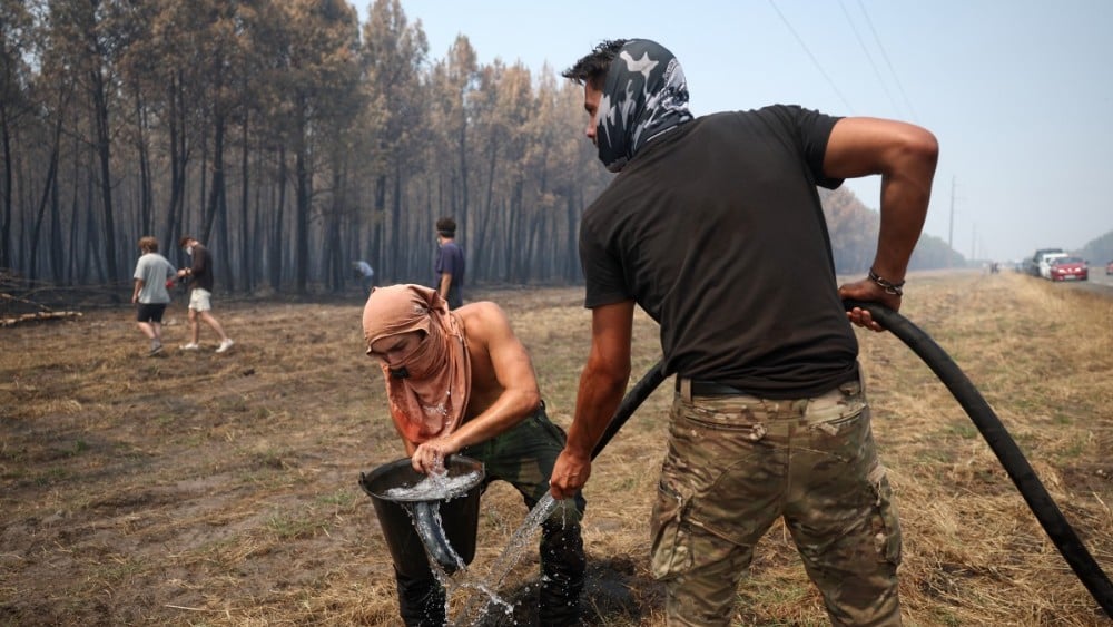 A volunteer fills a water bucket to help battle a forest fire in Lanton, west of Bordeaux, on July 29, 2026, amid wildfires in the Gironde region, southwestern France. (File photo: AFP)
