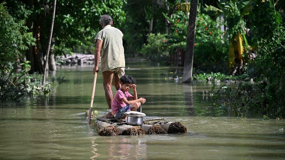 A girl and her grandfather travel on a raft through floodwaters following heavy monsoon rains at a village in Assam's Sivasagar district on July 27, 2026. (AFP)