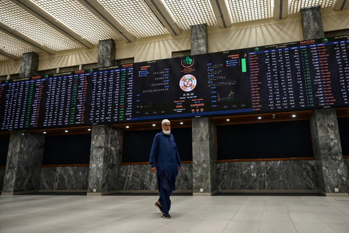 A stock broker walks past a digital board showing share prices at the Pakistan Stock Exchange (PSX) in Karachi on March 10, 2026. (AFP)