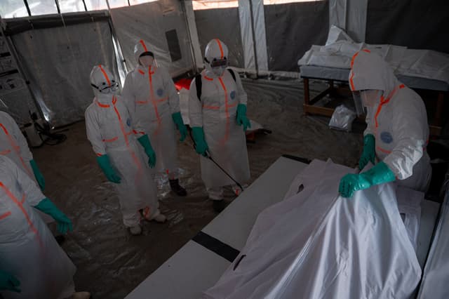 A team of doctors wearing protective suits works in a red zone inside the morgue, close a body bag containing the remains of a man who died from Ebola virus disease on June 13, 2026. (AFP)