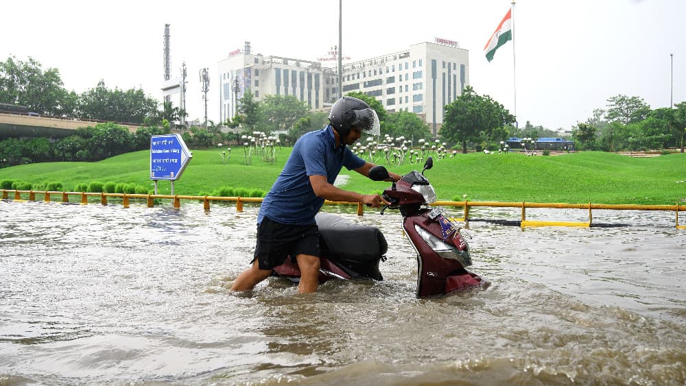A man pushes his scooter along a flooded road following heavy rainfall in New Delhi on August 25, 2026. (AFP)