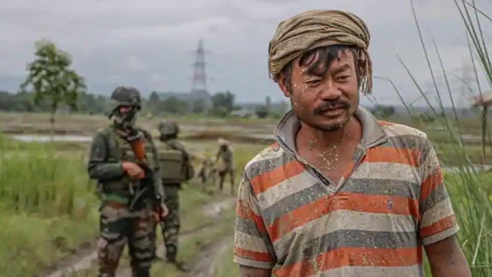 A farmer walks past security personnel at a paddy field in Imphal West, in India's northeastern state of Manipur on July 19, 2026, after cultivation disrupted by ongoing ethnic conflict resumed under tight security. (AFP)