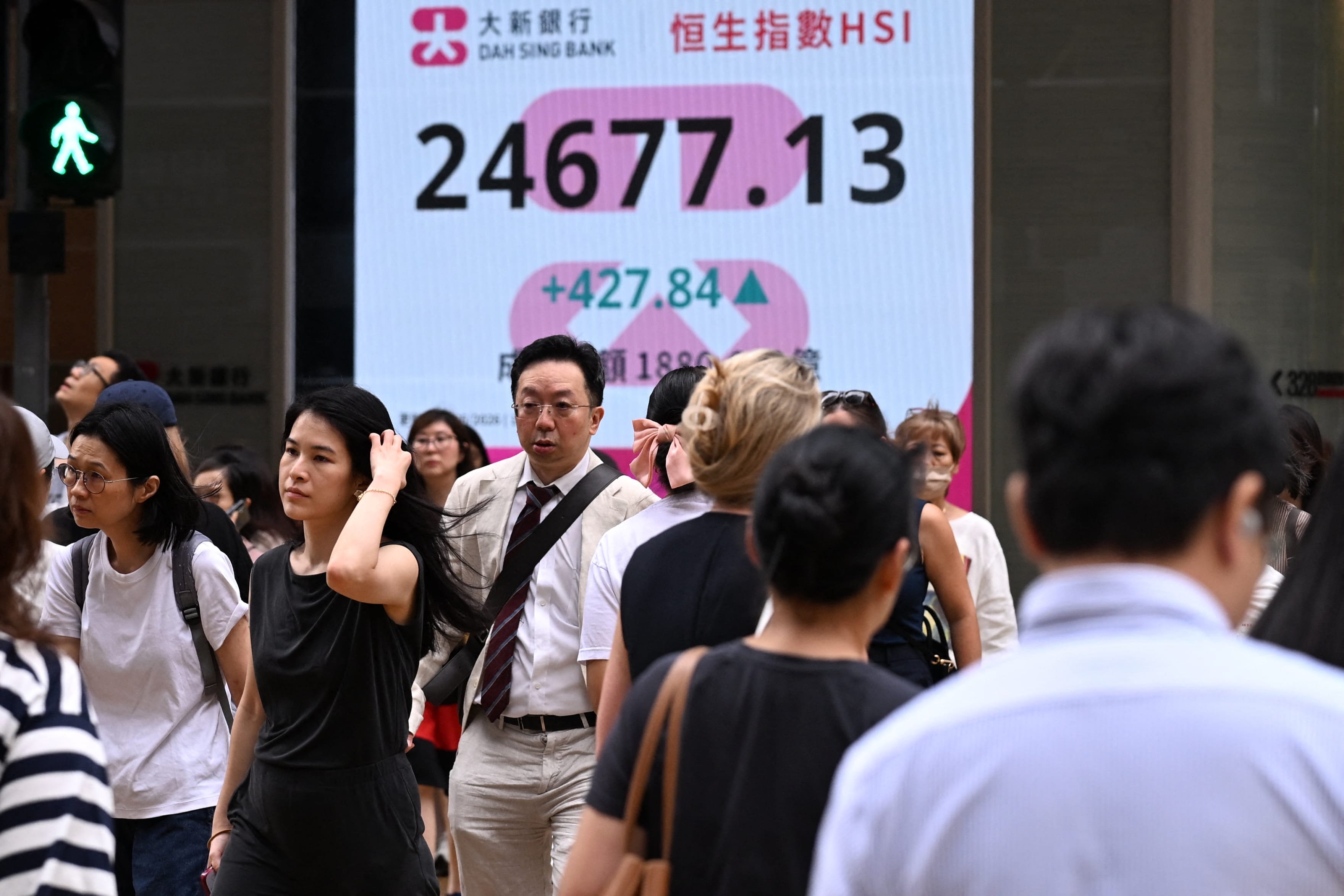 Pedestrians walk across a street next to an electronic sign board showing the Hang Seng Index in Hong Kong on June 12, 2026. (Photo by Peter PARKS / AFP)