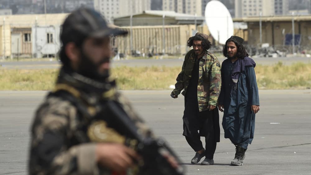 A member of the Taliban Badri 313 military unit (front) stands guard as two Taliban fighters walk inside the airport in Kabul. (AFP)