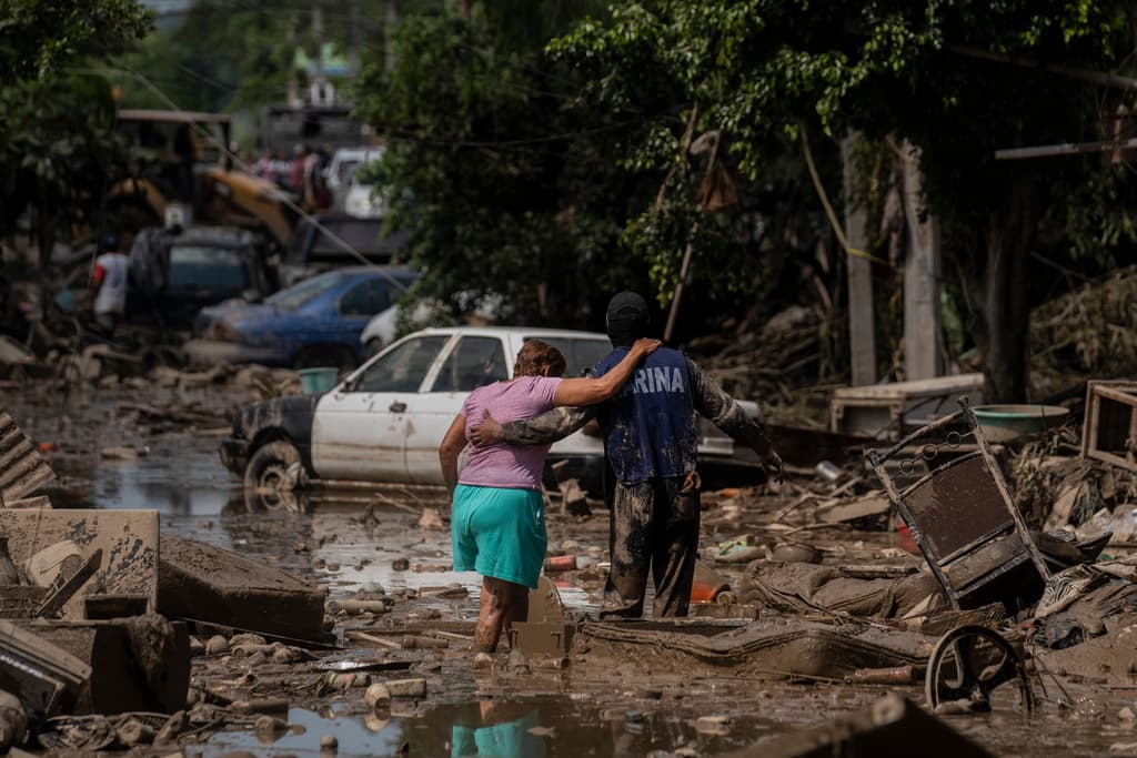 A Marine helps a woman cross a flooded street in Poza Rica, Veracruz state, Mexico, Sunday, Oct. 12, 2025. (AP Photo/Felix Marquez)