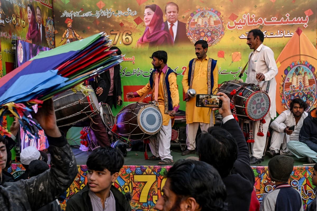 Artists play traditional drums next to a hoarding with portraits of Pakistan Muslim League Nawaz (PMLN) party leaders, as vendors sell kites to mark Basant Festival in Lahore on February 4, 2026. (Photo by Arif ALI / AFP)