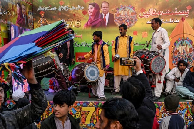 Artists play traditional drums next to a hoarding with portraits of Pakistan Muslim League Nawaz (PMLN) party leaders, as vendors sell kites to mark Basant Festival in Lahore on February 4, 2026. (Photo by Arif ALI / AFP)