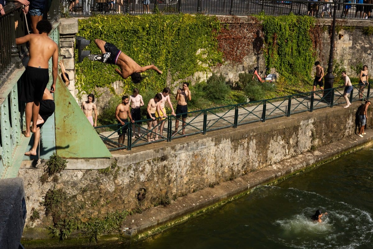 Swimmers jump from a bridge into the Canal Saint-Martin as France experiences a heatwave, in Paris on June 22, 2026 (AFP)