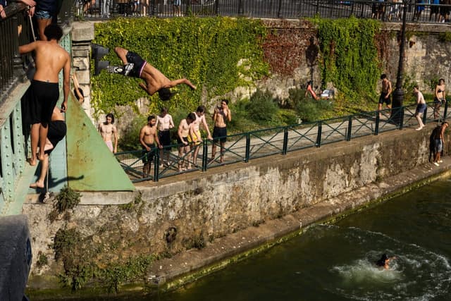 Swimmers jump from a bridge into the Canal Saint-Martin as France experiences a heatwave, in Paris on June 22, 2026 (AFP)