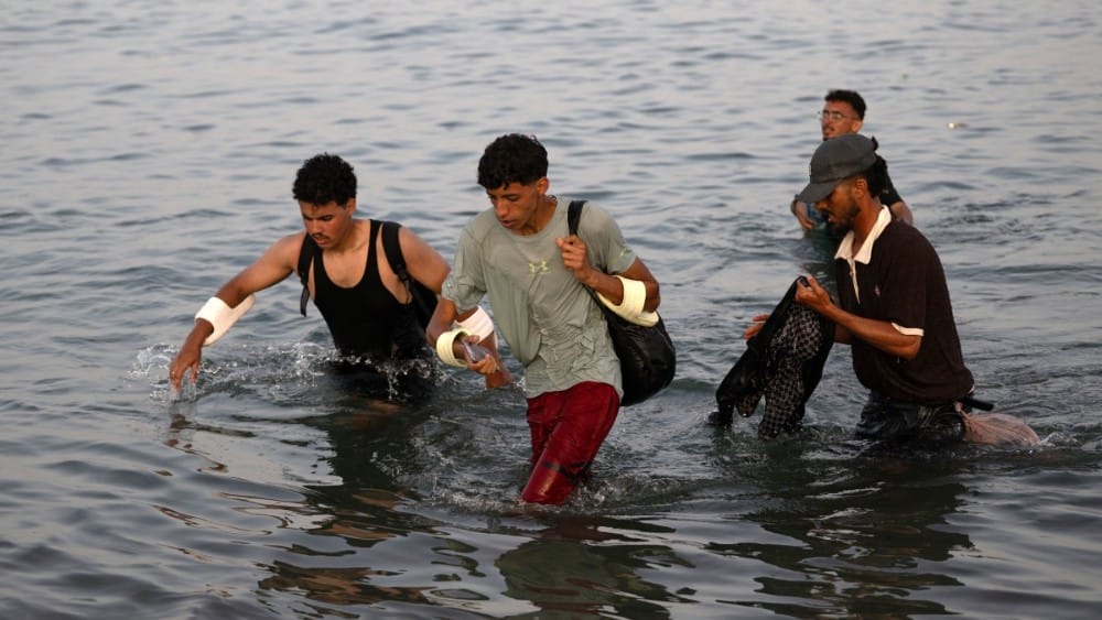 Migrants wade through the water near the border with Morocco as they attempt to enter Spain's North African enclave of Ceuta on July 31, 2026 (AFP)