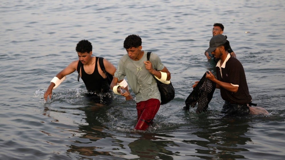 Migrants wade through the water near the border with Morocco as they attempt to enter Spain's North African enclave of Ceuta on July 31, 2026 (AFP)