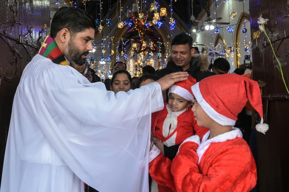 A priest blesses children dressed as Santa Claus on the occasion of Christmas at a church in Amritsar on December 25, 2025. (Photo by Narinder NANU / AFP)