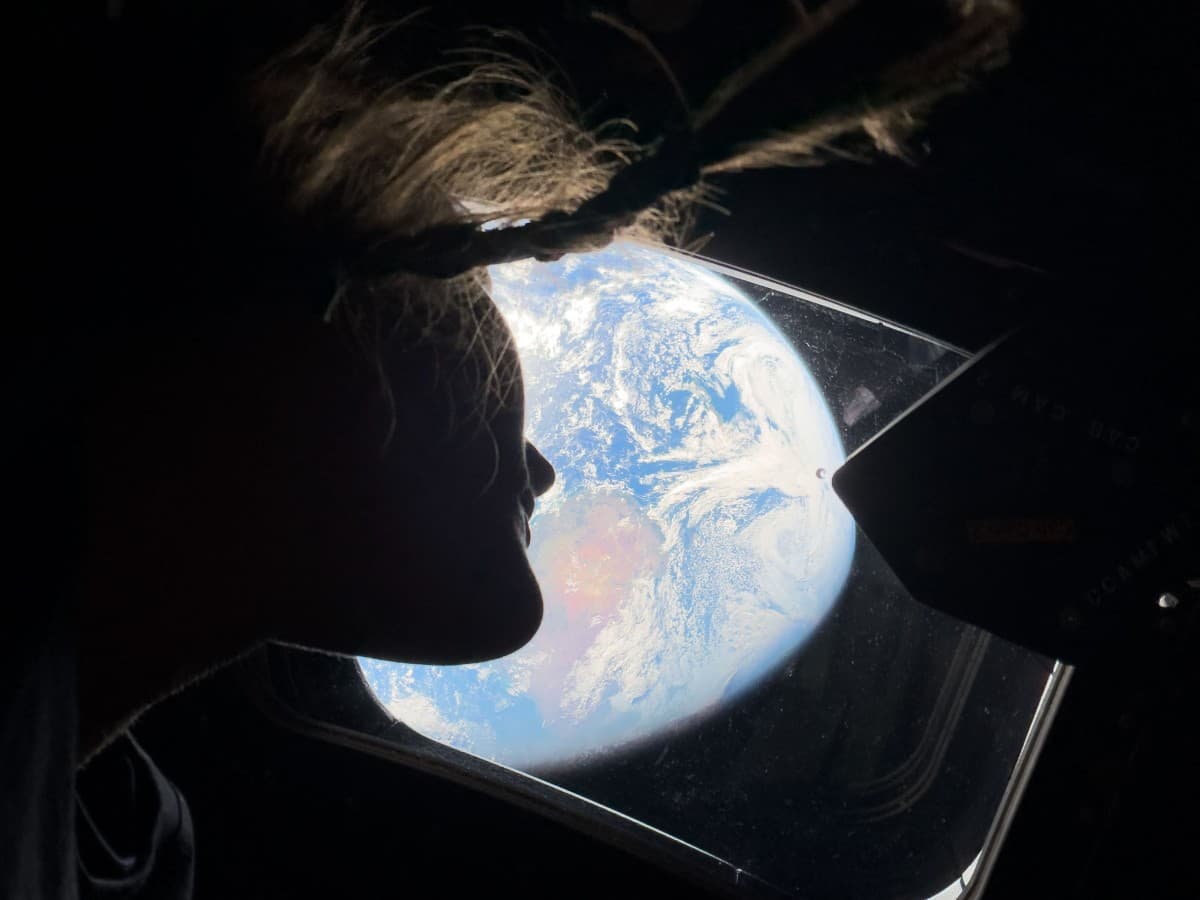 In this handout image provided by NASA, NASA astronaut and Artemis II mission specialist Christina Koch peers out of one of the Orion spacecraft's main cabin windows, looking back at Earth, as the crew travels towards the Moon on April 4, 2026. (IN SPACE/