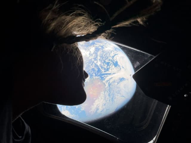 In this handout image provided by NASA, NASA astronaut and Artemis II mission specialist Christina Koch peers out of one of the Orion spacecraft's main cabin windows, looking back at Earth, as the crew travels towards the Moon on April 4, 2026. (IN SPACE/