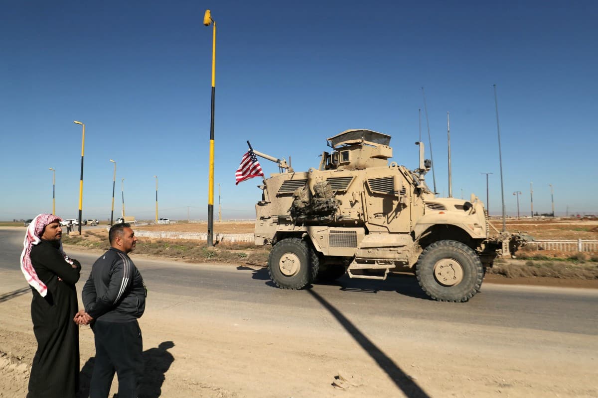 Men watch as a US military mine-resistant ambush protected (MRAP) armored fighting vehicle moves in a convoy along a highway outside Qamishli in Syria's northeastern Hasakah province on February 23, 2026. (AFP)
