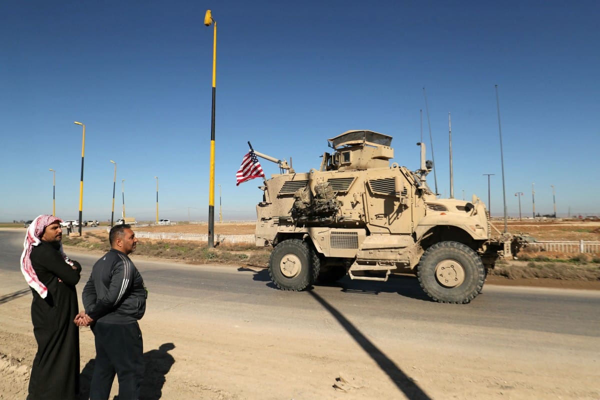 Men watch as a US military mine-resistant ambush protected (MRAP) armored fighting vehicle moves in a convoy along a highway outside Qamishli in Syria's northeastern Hasakah province on February 23, 2026. (AFP)