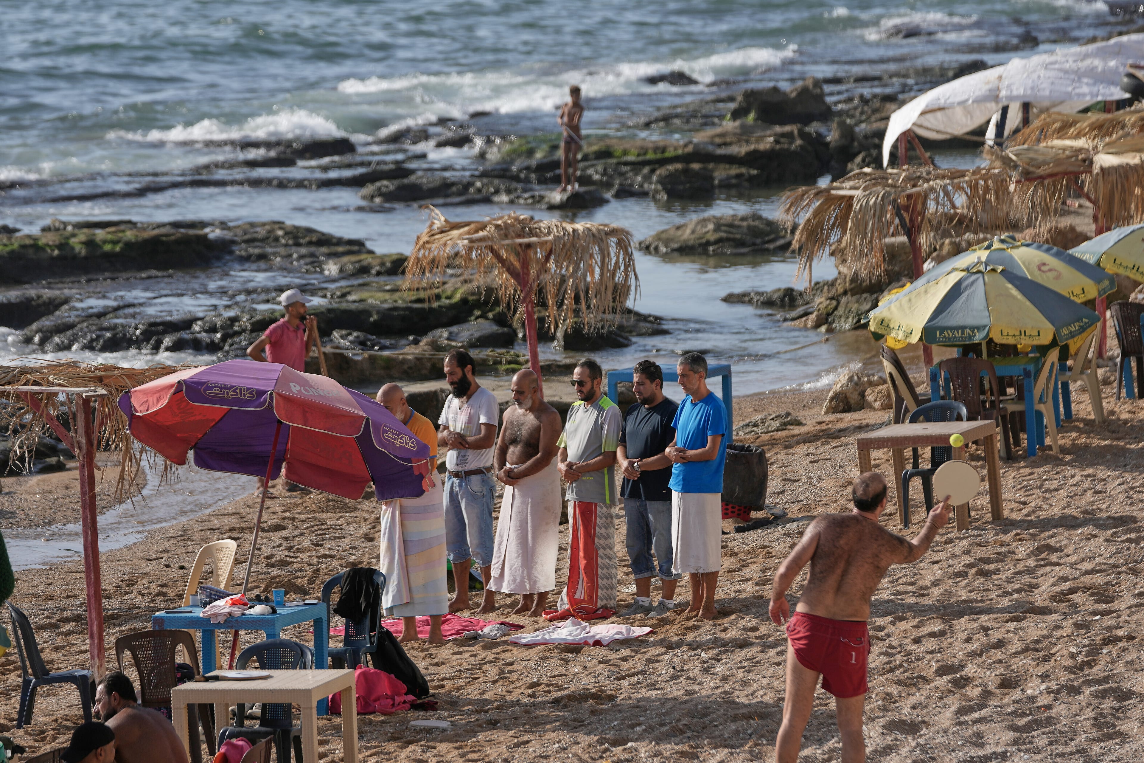 Syrian men attend their noon prayer, left, as others play racket ball at a public beach on the Mediterranean sea, in the coastal city of Latakia, Syria. (AP)