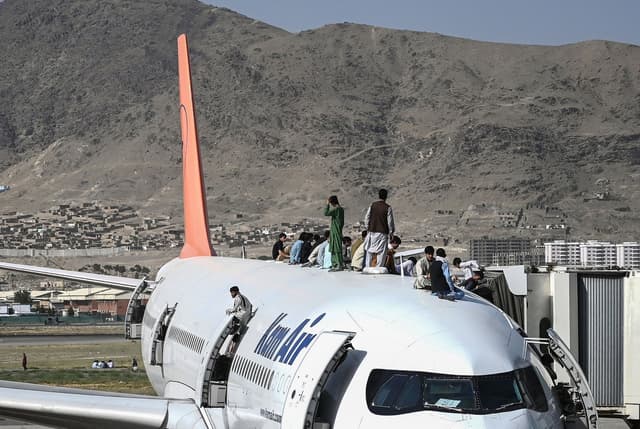 Afghan people climb atop a plane as they wait at the Kabul airport in Kabul on August 16, 2021, as thousands of people mobbed the city's airport trying to flee. (AFP)