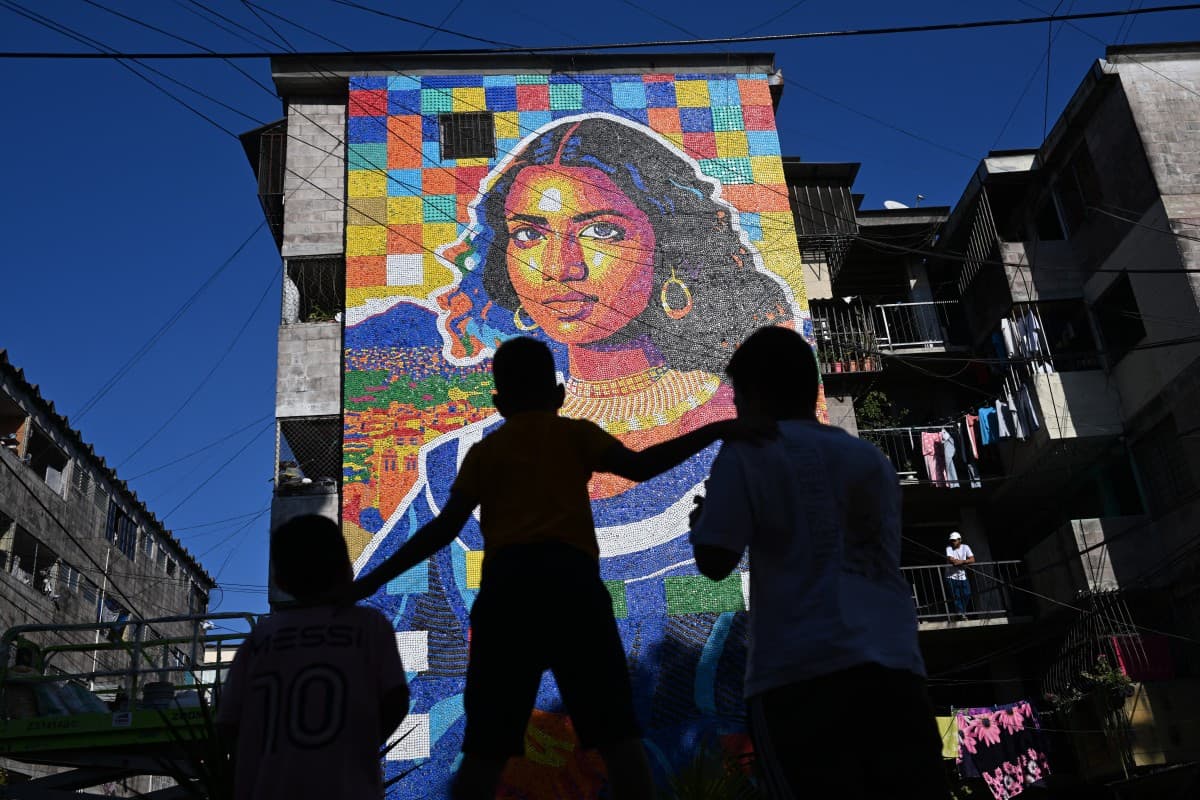 Children look at a mural made with plastic bottle caps by Venezuelan artist Oscar Olivares on an apartment building in the Zacamil neighborhood in Mejicanos, El Salvador, on February 20, 2026. (AFP)
