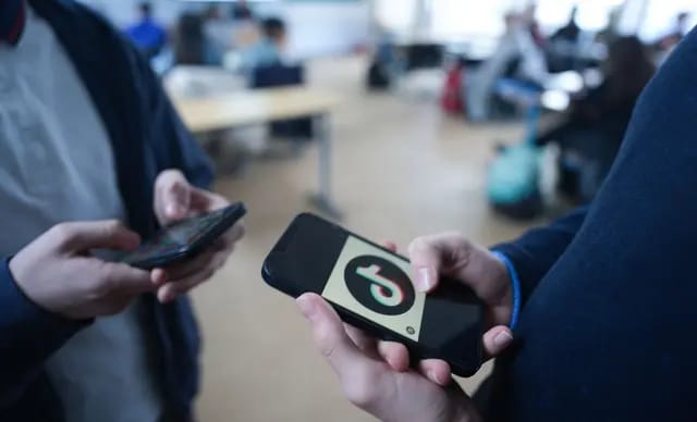 Two pupils stand in a classroom at Goethe-Gymnasium and look at their smartphones; the logo of the social media platform TikTok can be seen on one of the displays. (AFP)